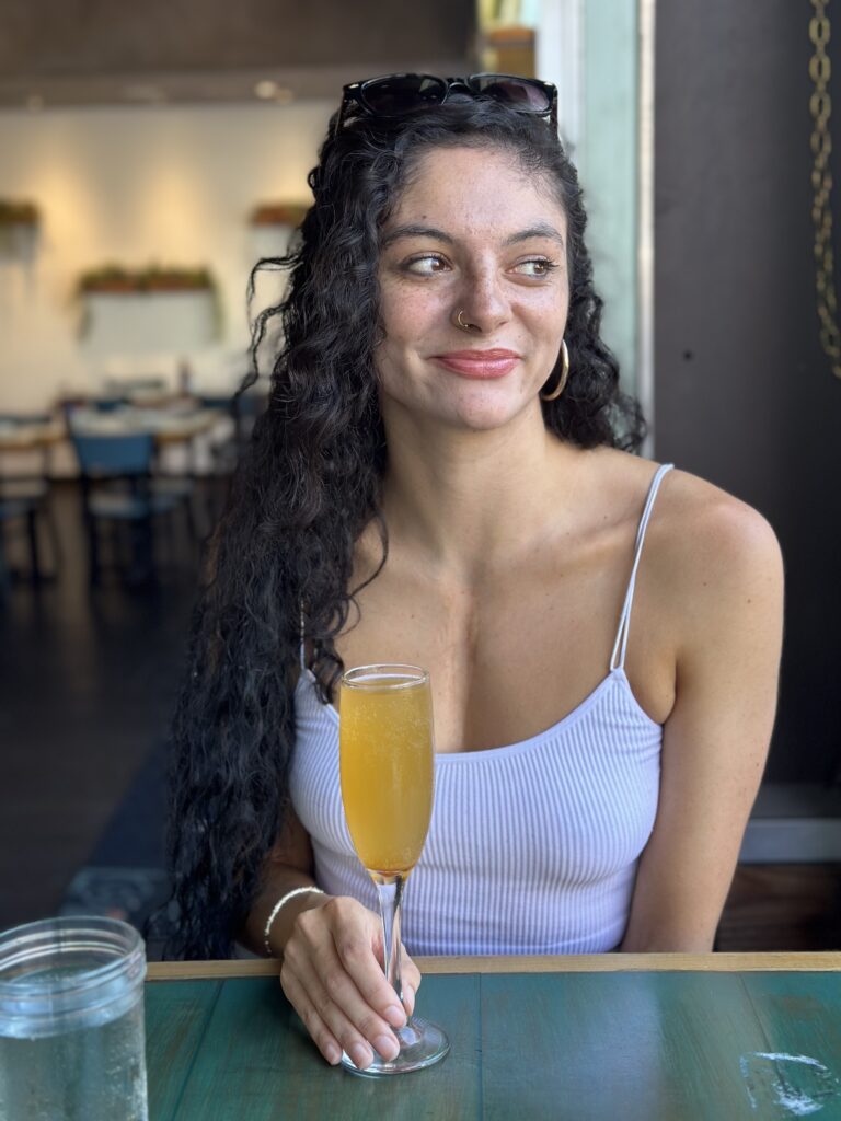 madi in a purple top with drink in hand looking away from the camera while smiling
